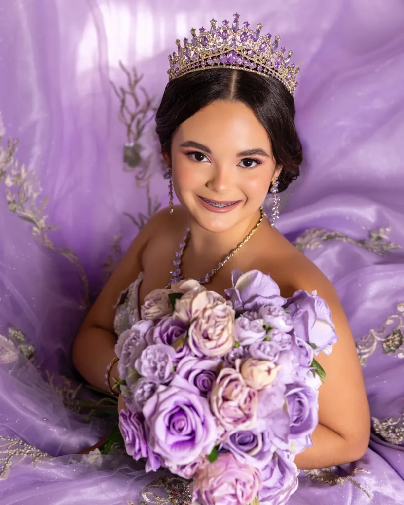 Quinceañera con vestido lila y corona, sosteniendo ramo de rosas moradas