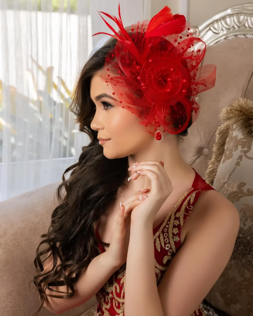 Chica con vestido rojo bordado y tocado de plumas posando en un sillón