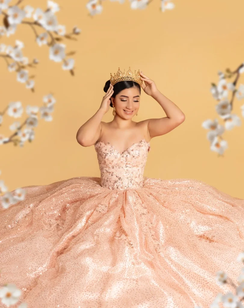 Quinceañera con vestido rosa brillante y corona dorada sobre fondo floral