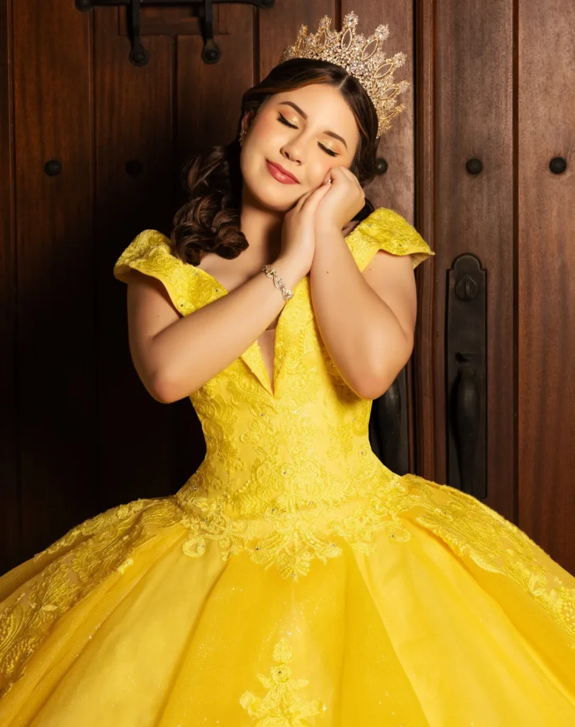 Quinceañera feliz con vestido amarillo y corona dorada en puerta rústica