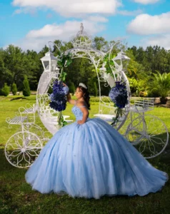 Quinceañera con vestido azul claro junto a carruaje decorado en jardín